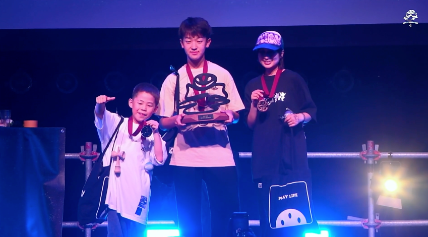 EKC 2026 Freestyle Division podium with winner Ryoga Kawamoto holding the first-place trophy, Naru in 2nd place, and Nonoka Kyodo in 3rd place celebrating with their medals on stage.