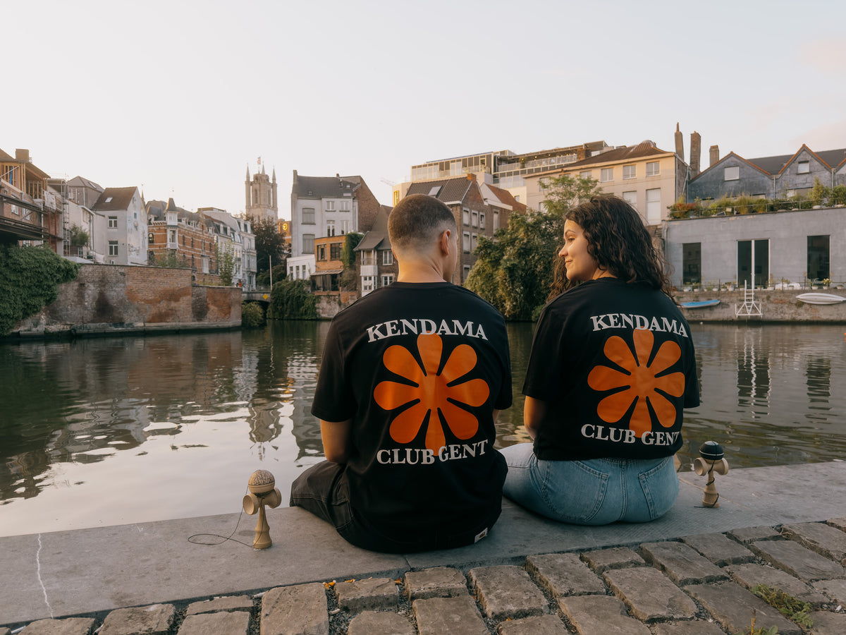 Two kendama players sitting by the canal in Ghent wearing KIN flower shirts
